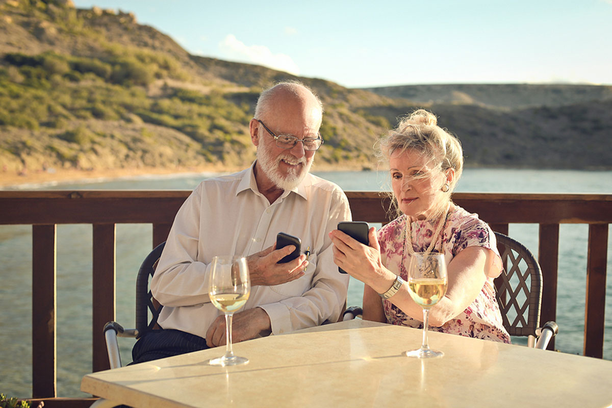 Elderly couple sitting beachside and looking at their phones