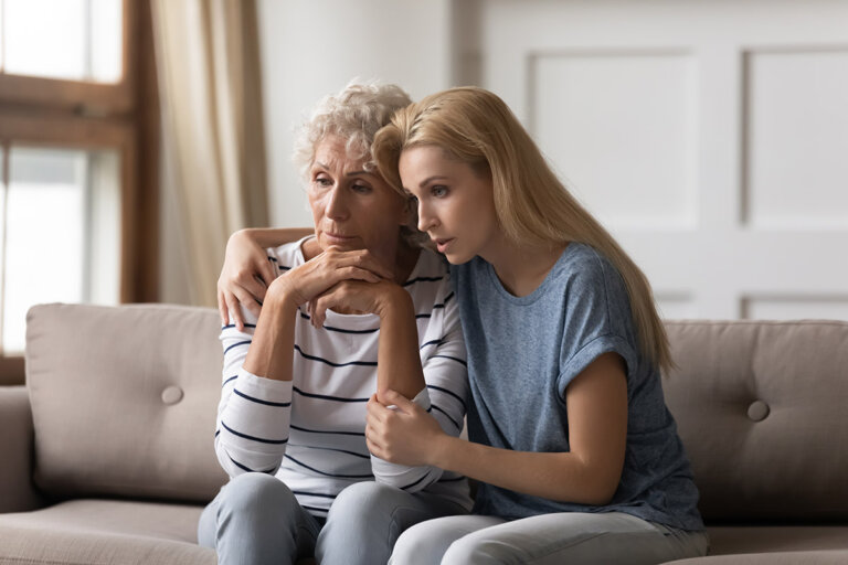 Elderly mother and her daughter sitting on a couch with a distressed look on their faces