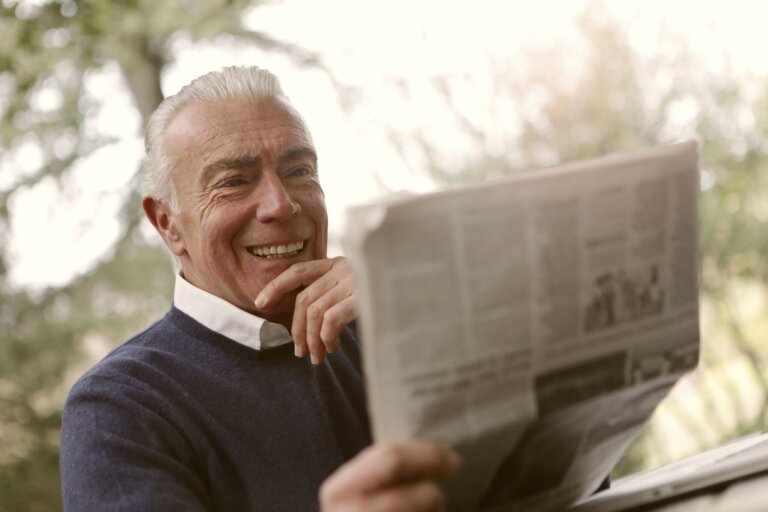 Elderly man reading the newspaper while laughing