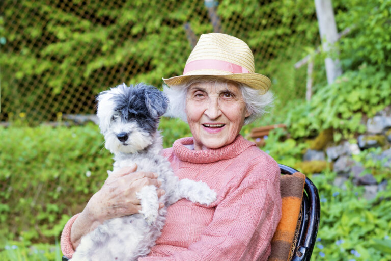 Elderly woman wearing a sunhat while holding her dog
