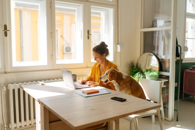 Woman sitting at her desk while her dog accompanies her